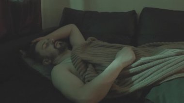 Bir adam kahverengi bir battaniyenin altında bir kanepede uyur. Konsept: Zihinsel endişe ve kararsızlık, zihinsel bozukluk.