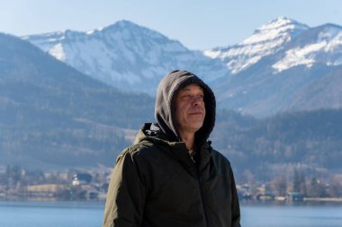 Orta yaşlı bir adam kar kaplı dağların arka planına gülümsüyor..