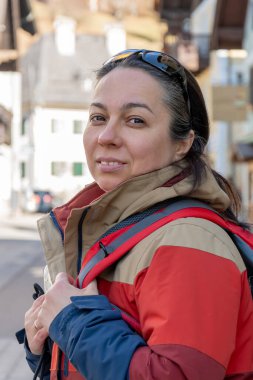 40-45 yaşlarında, sırt çantalı bir kadın turist dağlarda güzel bir kasabada yürüyor.