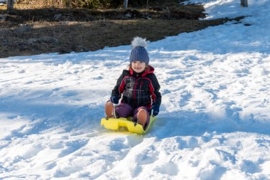 Neşeli bir çocuk karda kayıyor, kış eğlencesinin ve açık hava aktivitelerinin tadını çıkarıyor.