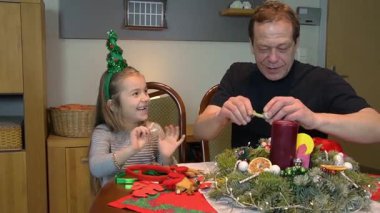 Baba ve kızı masada Noel çelengi süslüyor.