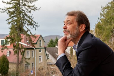 Sakallı şık bir beyefendi rahat bir Avrupa şehrinin arka planına bakarak hayal kuruyor.