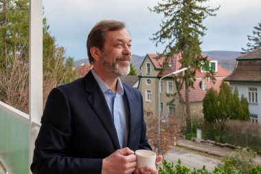 Avrupa 'da rahat bir evin arka planında bir fincan kahvesi olan klasik tarzda bir adam.