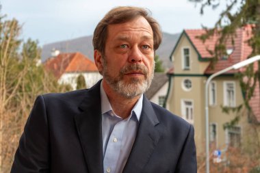 Klasik takım elbiseli olgun bir adamın portresi eski evlerin ve doğanın arka planına karşıdır.
