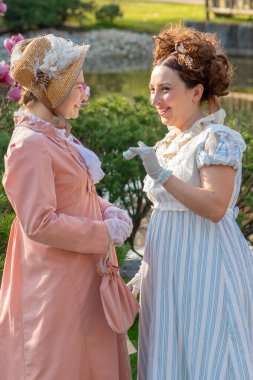 Tarihi kostümler içinde bahar bahçesinde sohbet eden iki naip kadın.