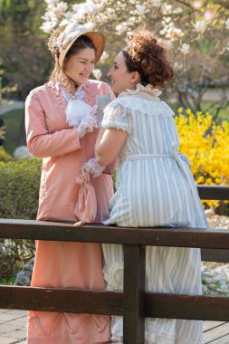 Gülümseme, klasik ve bahar - 19. yüzyıl kostümlü iki kadın köprüde sohbet ediyorlar