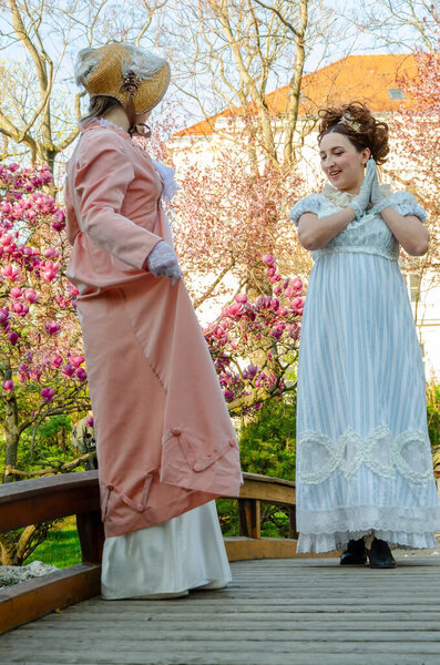 Historical reconstruction: two ladies in period costumes against a background of pink flowers