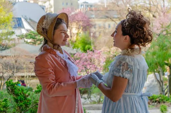 19. yüzyıl tarzı bir kadın arkadaşlığı. Çiçek açan ağaçların arasında fısıldaşıp sohbet ediyorlar.