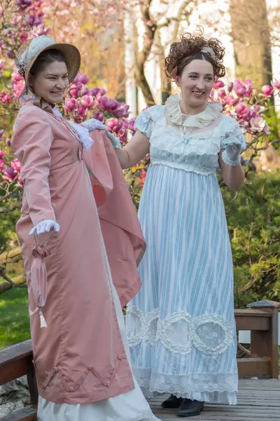 Geçmişten bir sahne. Eski moda giyinmiş kadınlar, çiçek açan manolya ağaçlarının arka planına karşı.