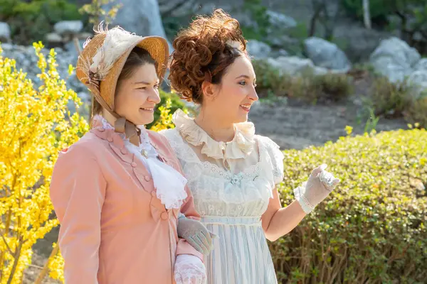 19. yüzyıl kostümlü iki orta yaşlı kadının bahar yürüyüşü: gülümseyen ve çiçek açan ağaçlar