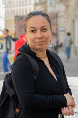 Sırt çantalı orta yaşlı bir kadın şehir caddesinde gülümsüyor.