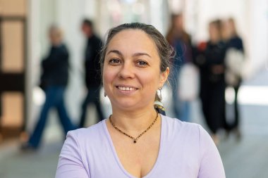 Şehir merkezinde duran 40-45 yaşlarında, siyah elbiseli bir kadının sakin portresi.