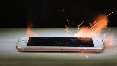 Masadaki akıllı telefon aşırı ısınma yüzünden yanıp sönüyor ve kıvılcımlar çıkıyor. Elektronik cihazların alev alması tehlikesi.