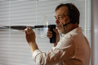 Penceresinde dinleme cihazı olan bir erkek casus. Kulaklık takan bir adam perdelerden yakından izler ve kulak misafiri olmak için yön mikrofonu kullanır.