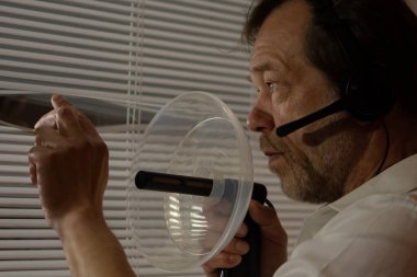 Casusluk. Bir adam profesyonel dinleme ekipmanları kullanır, jaluzilerden gözetler.