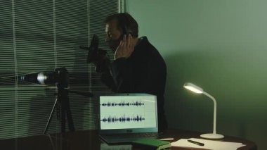 Karanlık bir odada bir adam, profesyonel bir kamera ve mikrofon kullanarak perdelerden gözetleme yapıyor.