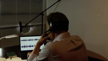 Gizli operasyon: Bir adam bir dizüstü bilgisayardaki ses kaydını masa lambasının loş ışığında analiz eder.