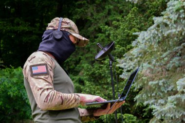 Kar maskesi takan ve kulaklık takan bir asker tarlada akustik sinyaller yakalar.