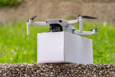 İnsansız hava aracıyla teslimat. Doğanın arka planında beyaz bir parsel olan bir dron. Çevre dostu ve hızlı teslimatın sembolü.