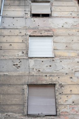 Hasarlı bir bina duvarına bariz bombardıman ve hasar belirtileriyle yakın plan. Alçıdaki delikler ve çipler açıkça savaş deneyimini ve yıkıcı etkilerini gösteriyor.