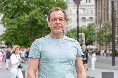 Şehir manzarasının arka planında yaşayan 50-55 yaşlarında modern bir adam. Şehir manzarası ve sokak hayatı arasında yetişkin bir adamın sakin ve kendinden emin görüntüsü.