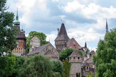 Sık yeşilliklerle çevrili kuleleri ve kuleleri olan pitoresk bir şatonun fotoğrafı. Mimarisi Gotik ve Romanca tarzındadır.