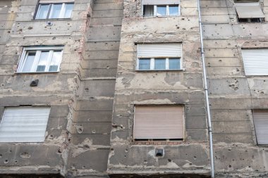 Savaşın izlerini taşıyan bir bina duvarı var. Birçok kurşun deliği ve tahrip edilmiş alçı savaş olaylarını ve kentsel çevre üzerindeki etkilerini güçlü bir şekilde hatırlatıyor.