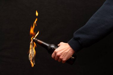 Bir adamın elindeki cam şişede yanan bir bez parçası, bir molotof kokteyli.