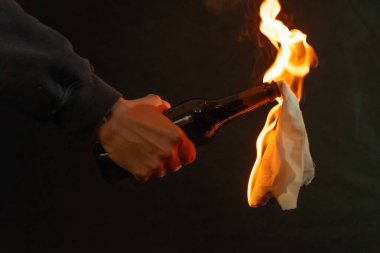 Karanlık bir arka planda yanan bir bez parçasıyla şişeyi tutan bir el - sokak protestosu veya çatışmasının sembolü