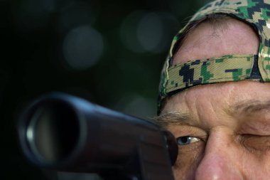 Kamuflaj şapkalı bir adam silah doğrultuyor. Avlanma, ateş etme ya da askeri eğitim kavramı