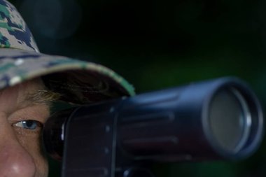 Piksel kamuflaj şapkalı bir adam tüfekle nişan alır. Temamız avcı, asker ya da keskin nişancı.