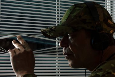 Gözetleme ya da gözetleme sahnesi - kamuflajlı bir adam kulaklıkla dinliyor ve pencereden izliyor.