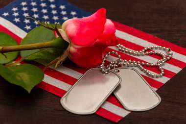 Kırmızı bir gül ve Amerikan bayrağının üzerinde duran asker künyesinin yakın çekimi, gazilerin ve şehit askerlerin anısına ve saygısını simgeliyor.