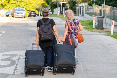 İki orta yaşlı ve yaşlı kadın bavulları ve bavullarıyla sessiz bir sokakta yürüyorlar.