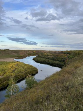 Nehrin ortasındaki bir kayanın üzerinde bir insan duruyor. Etrafı su, çimen ve bulutlu bir gökyüzünün altında. Doğal tabiat, akışkan araziler, göller ve düzlükler içerir.