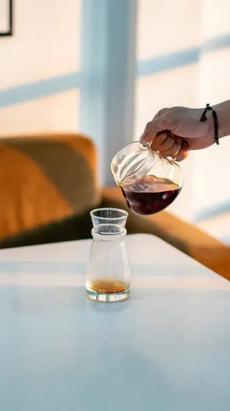 stock image A photo of coffee being poured from one server glass to another, held by a hand over a table. The image captures the smooth pouring motion, highlighting the rich coffee texture