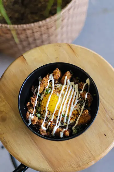 stock image rice with fried chicken and fried egg in black bowl on wooden table