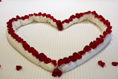 Bir otel yatağında gül yaprakları ve havlulardan oluşan bir kalp