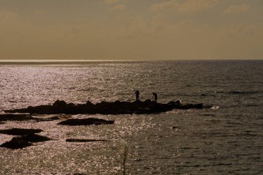 Akdeniz kıyısında gün batımında taştan balıkçıların siluetleri.