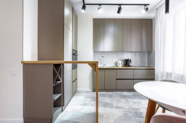 Pencere kenarındaki yemek pişirme alanında bir sürü dolap, tezgah, lavabo, mutfak aletleri mermer bir duvarın yanında..