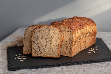 Tohumlu çavdar ekmeği açık bir masada, karanlık bir tahtanın üzerinde yatıyor. Ev pastanem. Organik tam tahıllı ekmek. Bio Dinkel Brot. Sağlıklı ekmek. Karbonhidratlar. Sağlıklı beslenme. Sağlıklı kahvaltı..