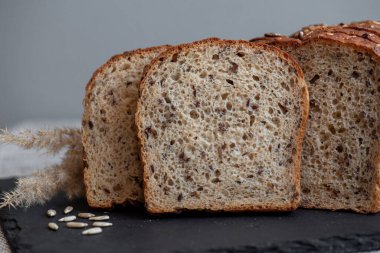 Tohumlu çavdar ekmeği açık bir masada, karanlık bir tahtanın üzerinde yatıyor. Ev pastanem. Organik tam tahıllı ekmek. Bio Dinkel Brot. Sağlıklı ekmek. Karbonhidratlar. Sağlıklı beslenme. Sağlıklı kahvaltı..