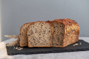 Tohumlu çavdar ekmeği açık bir masada, karanlık bir tahtanın üzerinde yatıyor. Ev pastanem. Organik tam tahıllı ekmek. Bio Dinkel Brot. Sağlıklı ekmek. Karbonhidratlar. Sağlıklı beslenme. Sağlıklı kahvaltı..