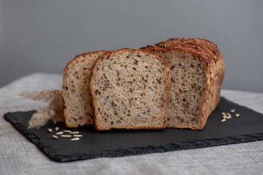 Tohumlu çavdar ekmeği açık bir masada, karanlık bir tahtanın üzerinde yatıyor. Ev pastanem. Organik tam tahıllı ekmek. Bio Dinkel Brot. Sağlıklı ekmek. Karbonhidratlar. Sağlıklı beslenme. Sağlıklı kahvaltı..