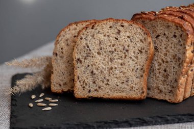 Tohumlu çavdar ekmeği açık bir masada, karanlık bir tahtanın üzerinde yatıyor. Ev pastanem. Organik tam tahıllı ekmek. Bio Dinkel Brot. Sağlıklı ekmek. Karbonhidratlar. Sağlıklı beslenme. Sağlıklı kahvaltı..