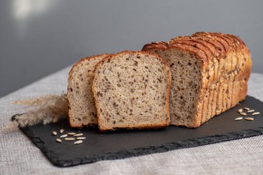 Tohumlu çavdar ekmeği açık bir masada, karanlık bir tahtanın üzerinde yatıyor. Ev pastanem. Organik tam tahıllı ekmek. Bio Dinkel Brot. Sağlıklı ekmek. Karbonhidratlar. Sağlıklı beslenme. Sağlıklı kahvaltı..