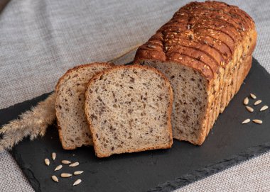 Tohumlu çavdar ekmeği açık bir masada, karanlık bir tahtanın üzerinde yatıyor. Ev pastanem. Organik tam tahıllı ekmek. Bio Dinkel Brot. Sağlıklı ekmek. Karbonhidratlar. Sağlıklı beslenme. Sağlıklı kahvaltı..