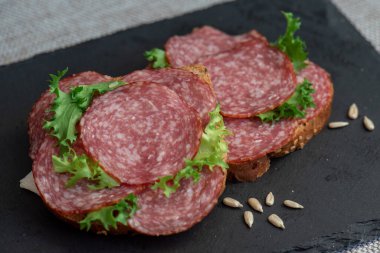 Siyah arka planda dilimlenmiş salam ve marul, üst manzara. Dilimlenmiş salamlı sandviç ve çavdar ekmeği.