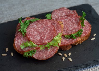 Siyah arka planda dilimlenmiş salam ve marul, üst manzara. Dilimlenmiş salamlı sandviç ve çavdar ekmeği.