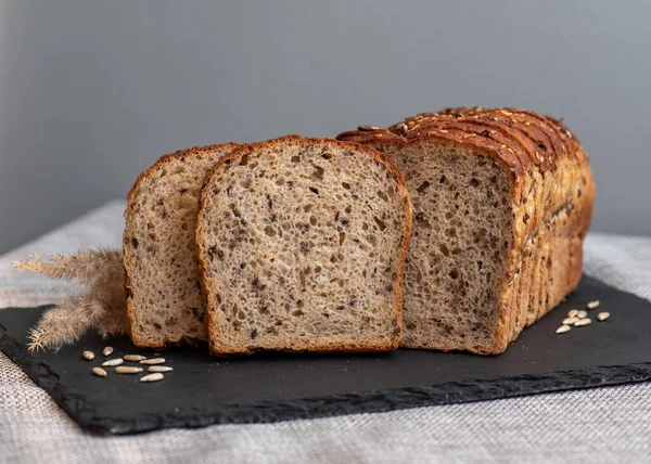 Tohumlu çavdar ekmeği açık bir masada, karanlık bir tahtanın üzerinde yatıyor. Ev pastanem. Organik tam tahıllı ekmek. Bio Dinkel Brot. Sağlıklı ekmek. Karbonhidratlar. Sağlıklı beslenme. Sağlıklı kahvaltı..